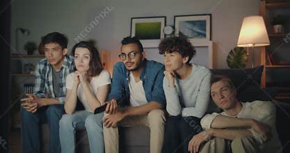 Bored friends choosing TV program clicking remote control at home at night