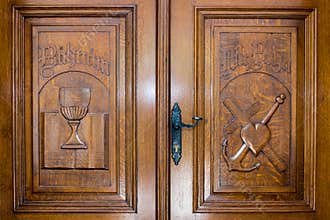 Wooden door with christian symbols: Bible, medieval cup, heart, cross and anchor