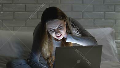 Female working on laptop in bed at night, suffering from neckache, bad posture