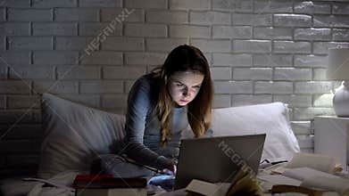 Female student among books typing project on laptop late at night, deadline