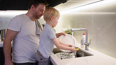 Little boy washing dirty dishes. Child cleans crockery while doing cleaning at home.