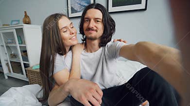 POV of man and woman taking selfie at home in bed holding camera kissing