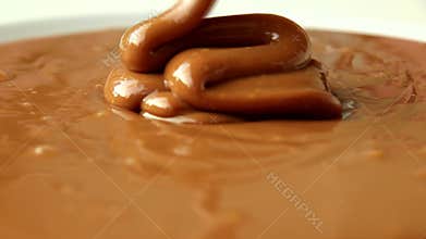 Liquid caramel pouring, dripping thick strand. Slow motion.