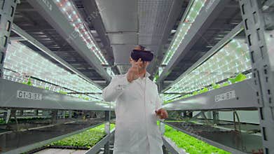 Male scientist in a white coat standing in the hallway of vertical farming with hydroponics with glasses virtualnoy