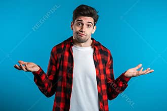 Young handsome unsure guy in red plaid shirt shrugs his arms