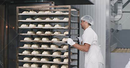 Process of loading the baking bread into the industrial oven , bakery worker load the big shelves beside him the food