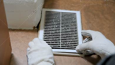 Man in gloves opens a dusty ventilation grill