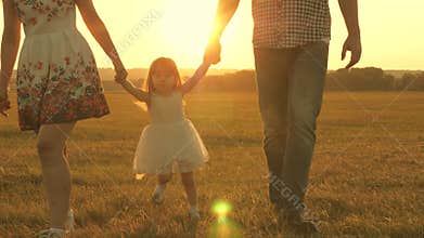 Little daughter jumping holding hands of dad and mom in park on background of sun. Family concept. child plays with dad