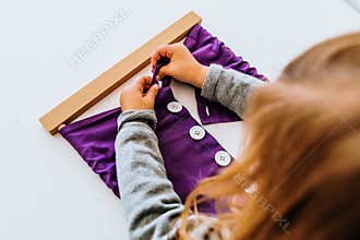 Girl buttoning a montessori frame to develop the dexterity of her fingers