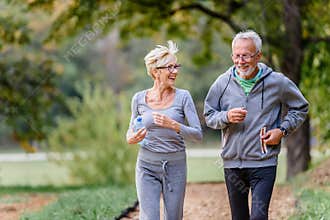 Cheerful active senior couple jogging in the park
