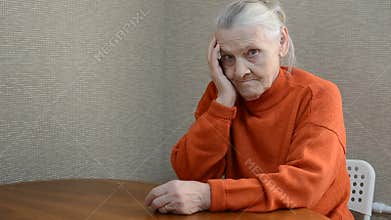 A lonely elderly woman sits at a table and holds her head sad from negative emotions