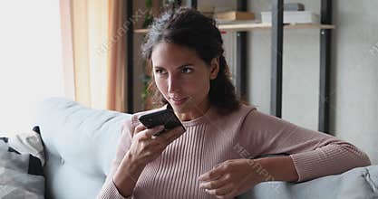 Smiling young woman using voice assistant on smartphone at home
