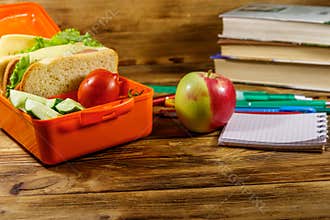 Back to school concept. School supplies, books, apple and lunch box with sandwiches and fresh vegetables on wooden desk