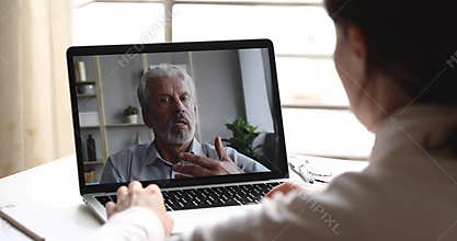 Serious old male psychologist consulting female client via webcam chat