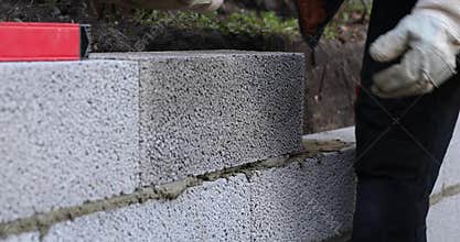 Mason working with ceramsite concrete blocks, building retaining wall