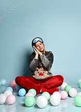 Teen girl in reindeer pajamas, red socks, sleep mask. closed eyes, sitting on floor, balloons, blue background. Close up