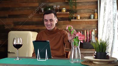 Romantic smiling young man presents beautiful flower through tablet to his girlfriend during online communication.