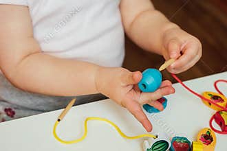 Child putting beads on a string. Bead stringing activity. Fine motor skills development
