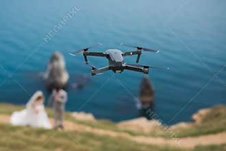 A drone photographs the bride and groom on a cliff near the sea