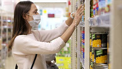 Young woman with child girl in medical masks buys a canned food at supermarket