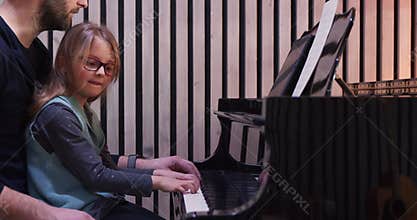 Dad teaching piano to his daughter.Little girl learning piano at home-Side view.Piano class at home. Child learning