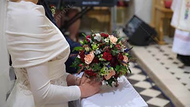 Bride is praying in the church holding the wedding bouquet in her hands.