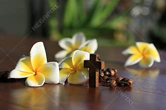 Wooden rosary with Jesus Christ holy cross crucifix and Bali frangipani flowers decoration background. Catholic symbol.