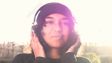 African American girl teenager young woman wearing a black beanie hat listening to music on headphones backlit by the sun