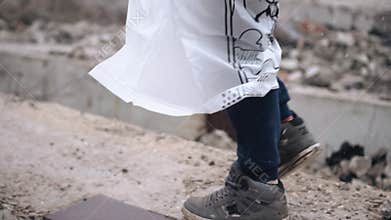A boy in a raincoat walks on concrete blocks from a destroyed house