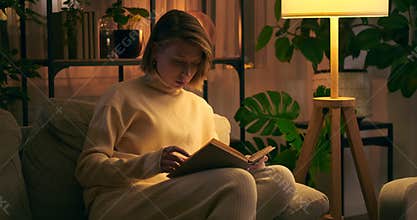 Woman reading a book on sofa at night