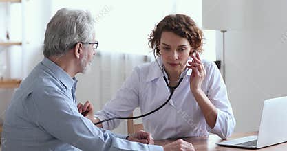 Female doctor holding stethoscope examining senior patient in hospital