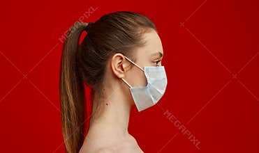 A young girl in a medical mask on a red background. Poster about the coronavirus COVID-19 pandemic.