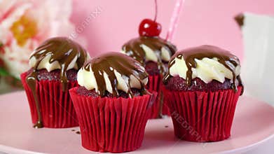 Red velvet cupcakes with chocolate sauce and cherries.