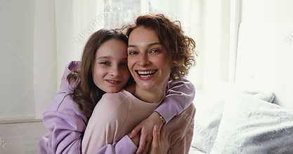 Happy adolescent child girl cuddling back of smiling mother.