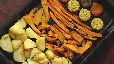 Baked vegetables and falafel. Potatoes, carrot and sweet potatoes on metal tray.