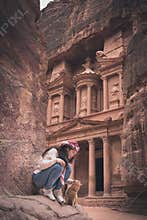 Young Asian traveller with cat sitting on rock in front of the Treasury or or Al-khazneh in Petra ruin and ancient city of