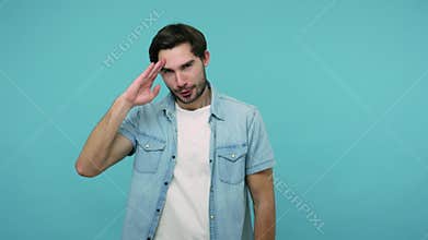 Positive bearded guy saluting with hand saying yes sir and looking at camera with humorous mockery expression