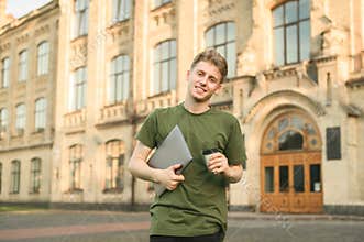Smiling young student man holding laptop computer looking at camera on a university background. Confident young smiling male
