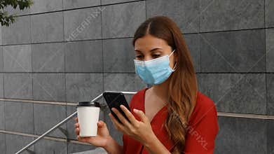 Young business woman with surgical mask holding coffee cup and using her phone while standing outside office building