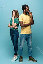 Length view of thoughtful interracial couple standing back to back on blue background