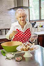 Happy senior woman decorating cupcakes in a bright modern kitchen