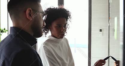 African female mentor training arab employee drawing on glass wall