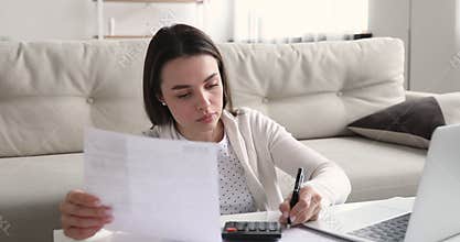 Concentrated young woman holding paper receipt, using e-banking application.