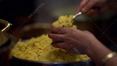 Woman is taking traditional indian rice from large pan