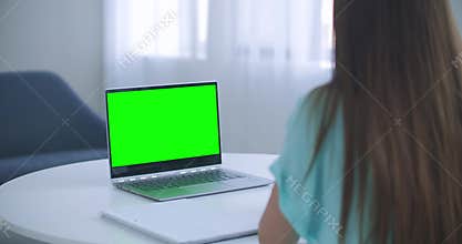 Girl taking notes in notepad from laptop computer Green Mockup Screen. Girl learning online on computer