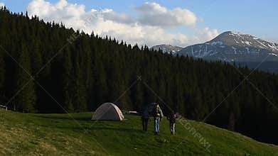 Three friends with backpacks go to the tent town in the mountains.