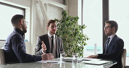 Diverse male colleagues celebrating agreement, shaking hands in office.