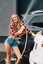 Girl holding pressure washer and smiling near autos