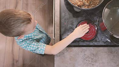 Child reaches for hot electric stove on kitchen. Kid burn danger