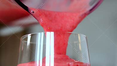 Pouring strawberry smoothies in glass from blender cup, close-up view in slow motion